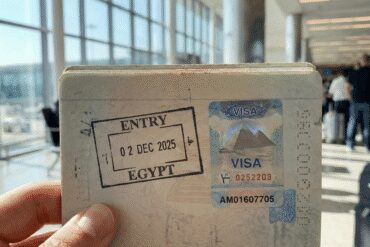 Close-up of an open passport with an Egyptian entry visa sticker and immigration stamp, held by a traveler in an airport.